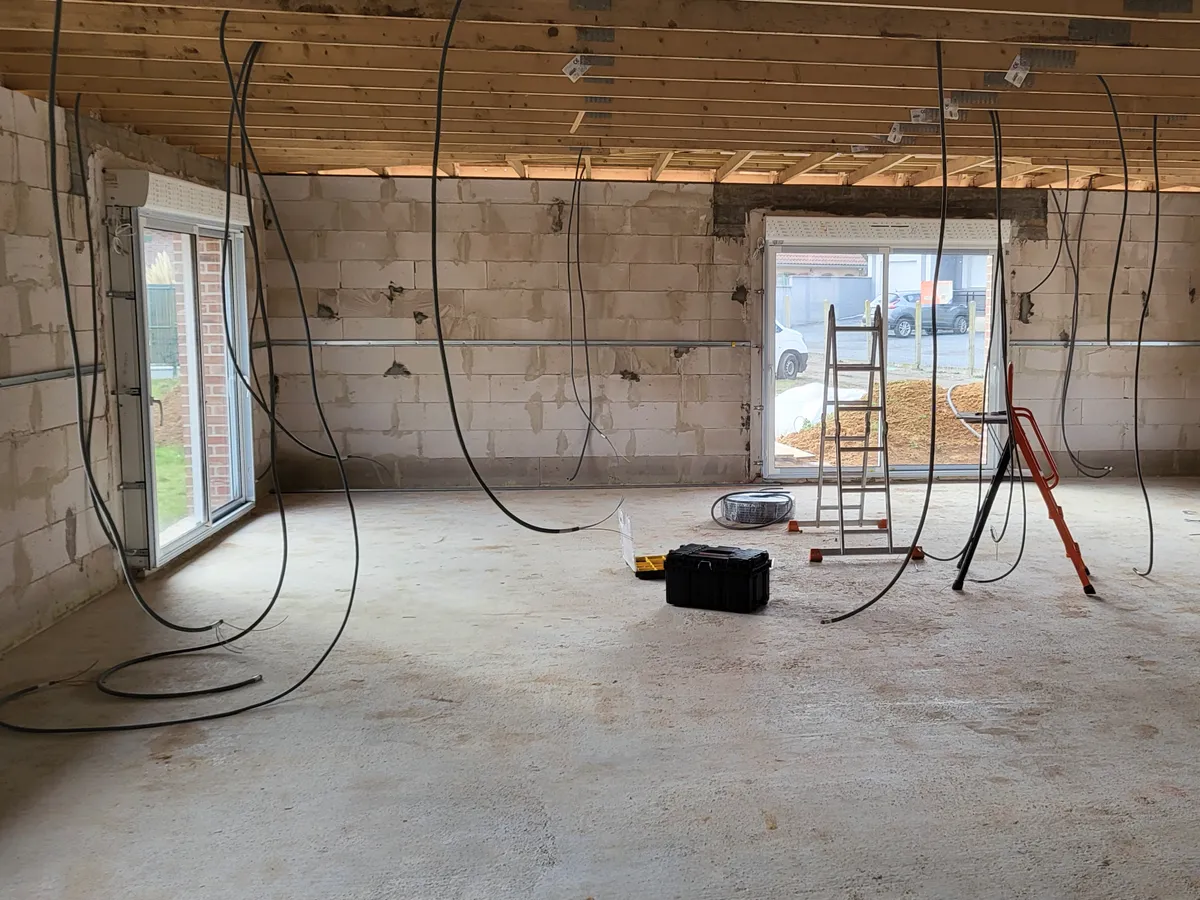 Pièce en cours de rénovation électrique : murs en parpaing, câbles électriques en attente au plafond.